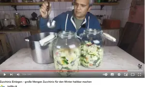 Mann füllt mit Schöpfkelle klein geschnittene Zucchini in Einmachgläser. Zucchini einwecken für den Winter.