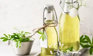 Zwei Flaschen mit hellem, gelbem Waldmeister Sirup, verziert mit frischen Waldmeisterzweigen und kleinen weißen Blüten.