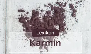 Ein Haufen echtes Karmin-Pulver, das auf einer hellen Oberfläche verstreut ist. Der Text "Lexikon Karmin" ist überlagert.