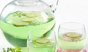 Erfrischendes Getränk mit Limettenscheiben und Waldmeister-Zweigen in einer Karaffe und Gläsern. Perfekt für Waldmeister Rezepte.