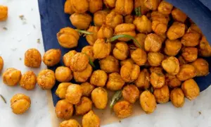 Knuspriger kichererbsen snack, gewürzt und mit Rosmarin verfeinert, liegt auf einem blauen Tuch und Marmor.