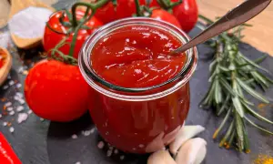 Frisches, selbstgemachtes Ketchup in einem Glas, umgeben von reifen Tomaten, Knoblauch und Rosmarin. Perfekt zum Ketchup selber machen!