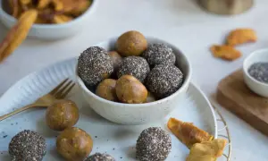 Schale mit gesunden Energiebällchen, einige in Chiasamen gerollt, andere pur. Getrocknete Mangostücke liegen daneben.