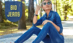 Frau in Jeansjacke und Hose, die entspannt im Park sitzt. "BIO JEANS" Schriftzug deutet auf nachhaltige deutsche Jeansmarken hin.