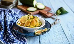 Knusprige Zucchini-Chips in einer Schüssel, daneben frische Zucchinischeiben auf einem Holzbrett.