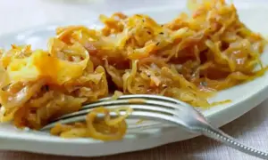 Ein Teller mit goldbraunem, gedünstetem Sauerkraut, das gerade mit einer Gabel serviert wird. Perfekt zum Sauerkraut kochen.