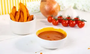 Süßkartoffel-Pommes mit selbstgemachtem Ketchup ohne Zucker. Zutaten wie Tomaten, Zwiebel und Knoblauch sind zu sehen.