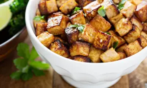 Knusprig gebratene Tofuwürfel, perfekt zum tofu zubereiten, garniert mit Petersilie und Sesam. Daneben ein Schälchen mit Brokkoli und Limette.