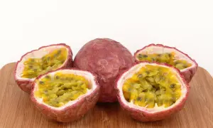 Ein ganzes und drei halbierte Passionsfrüchte liegen auf einem Holzbrett. Das Fruchtfleisch mit den Kernen lädt zum Passionsfrucht essen ein.