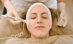 Eine Kosmetikerin trägt mit einem Pinsel eine Maske auf das Gesicht einer Frau auf, um es zu reinigen.