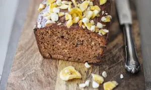Saftiger bananenkuchen vegan mit Schokoladenglasur und Nüssen, auf einem Holzbrett mit einem Messer.