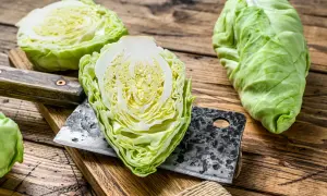 Frischer Spitzkohl, halbiert und auf einem Holzbrett mit einem Hackmesser. Perfekt, um Spitzkohl roh zu essen, als knackiger Salat.