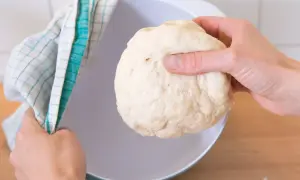 Hefeteig einfrieren: Eine Hand hält den Teig, die andere bedeckt eine Schüssel mit einem Küchentuch.