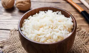 Schüssel mit frisch gekochtem Naturreis, daneben Walnüsse und Kochutensilien. Perfekt für eine gesunde Mahlzeit.