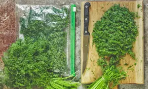 Frischer Dill wird gehackt und in einem Beutel zum **Dill trocknen** aufbewahrt. Ein Messer liegt neben dem Dill auf einem Holzbrett.