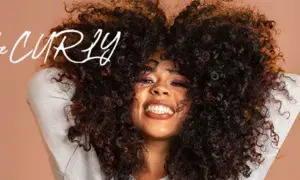 Frau mit vollem, lockigem Haar, die lächelt. Der Schriftzug "be CURLY" ist im Bild zu sehen.