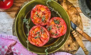 Drei saftige Scheiben Tomaten, perfekt gegrillt und mit frischen Kräutern bestreut, liegen auf einem grünen Teller. Ein Genuss für alle Sinne!