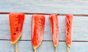 Vier gefrorene Wassermelonenstücke auf Holzstäbchen. Man kann Wassermelone einfrieren und so erfrischende Snacks für heiße Tage kreieren.