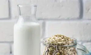 Glasflasche mit weißer Flüssigkeit neben einem Glas voller Haferflocken. Perfekt, um Hafermilch selber zu machen.