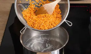 Rote Linsen werden aus einem Sieb in kochendes Wasser geschüttet. Das Kochen von Linsen ist einfach und schnell.