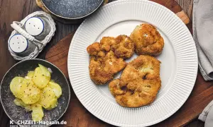 Knusprig **gebratener Blumenkohl** auf einem weißen Teller, daneben Kartoffelsalat und ein Salz- und Pfefferstreuer.