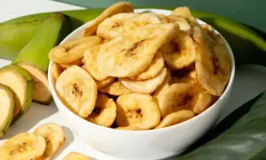 Schmackhafte bananenchips selber machen ist ganz einfach. Hier sind sie in einer Schüssel, daneben grüne Bananen und Blätter.
