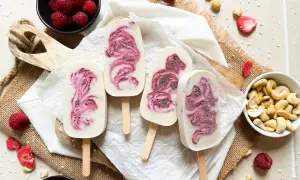 Eis am Stiel mit Himbeermuster, inspiriert von einfachen eis rezepte. Frische Himbeeren und Cashewkerne liegen daneben.
