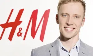 Junger Mann lächelt vor H&M-Logo. Kritische Stimmen werfen dem Unternehmen H&M Greenwashing vor, während es sich als nachhaltig präsentiert.