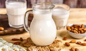 Frisch zubereitete Mandelmilch in einer Glaskaraffe, daneben Gläser und eine Schale mit Mandeln. So einfach ist Mandelmilch selber machen!