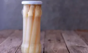 Ein Glas mit eingelegtem weißen Spargel steht auf einem Holztisch. Perfekt für das Spargel einkochen.