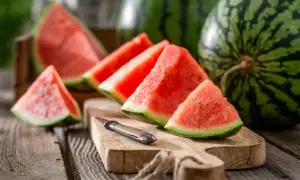 Saftige Wassermelonenstücke auf einem Holzbrett, daneben ganze Früchte. Die Wassermelone ist ein Sommergenuss, ihre Haltbarkeit ist bei richtiger Lagerung gut.