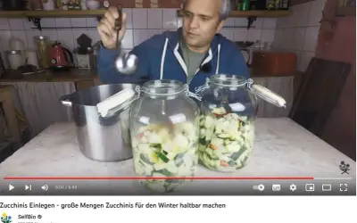 Mann füllt mit Schöpfkelle klein geschnittene Zucchini in Einmachgläser. Zucchini einwecken für den Winter.