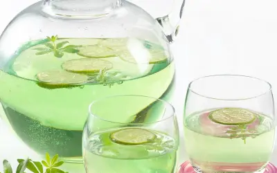 Erfrischendes Getränk mit Limettenscheiben und Waldmeister-Zweigen in einer Karaffe und Gläsern. Perfekt für Waldmeister Rezepte.