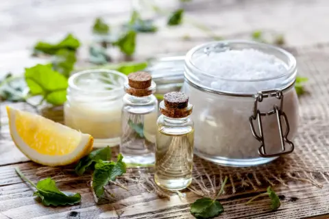 Zutaten für kosmetik selber machen: Zitrone, ätherische Öle, Salz und Kräuter auf Holzuntergrund.