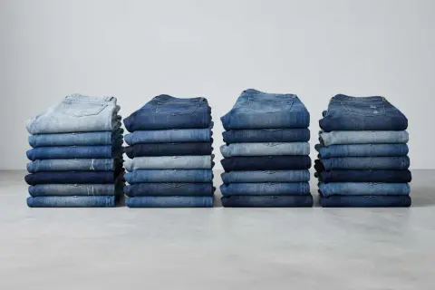 Stapel von Jeanshosen in verschiedenen Blautönen. Sie zeigen, aus was Jeans bestehen: robustem Denim-Stoff.