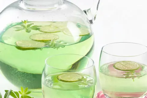 Erfrischendes Getränk mit Limettenscheiben und Waldmeister-Zweigen in einer Karaffe und Gläsern. Perfekt für Waldmeister Rezepte.