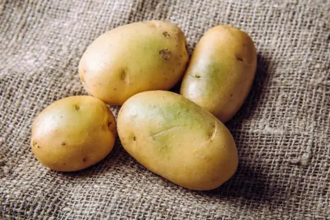 Vier frische Kartoffeln liegen auf grobem Leinen. Perfekt, um sie mit Schale zu essen und die Vitamine zu genießen.