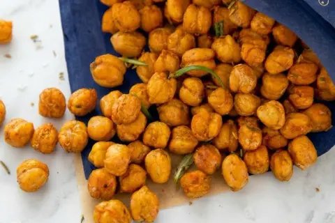 Knuspriger kichererbsen snack, gewürzt und mit Rosmarin verfeinert, liegt auf einem blauen Tuch und Marmor.