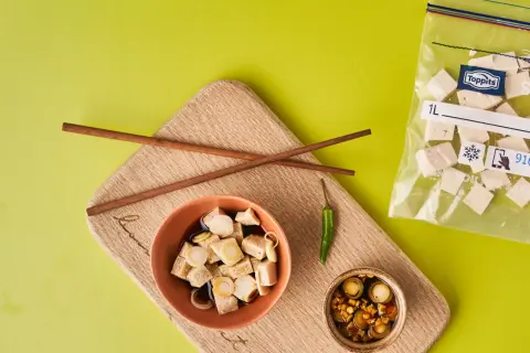 Vorbereitung für tofu einfrieren: gewürfelter Tofu in Schüssel mit Soße, daneben ein kleiner Chili und ein Beutel mit gefrorenem Tofu.