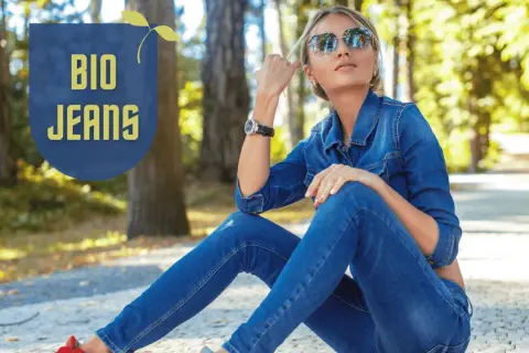 Frau in Jeansjacke und Hose, die entspannt im Park sitzt. "BIO JEANS" Schriftzug deutet auf nachhaltige deutsche Jeansmarken hin.
