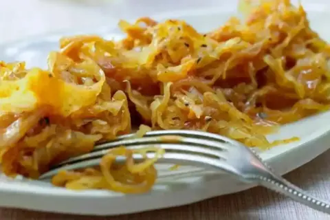 Ein Teller mit goldbraunem, gedünstetem Sauerkraut, das gerade mit einer Gabel serviert wird. Perfekt zum Sauerkraut kochen.