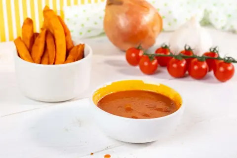 Süßkartoffel-Pommes mit selbstgemachtem Ketchup ohne Zucker. Zutaten wie Tomaten, Zwiebel und Knoblauch sind zu sehen.