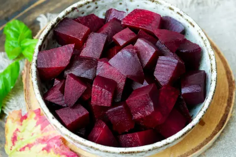 Schüssel mit gewürfelter roter Bete, die nach dem Kochen mit Essig glänzt. Ein Hauch von Herbst mit Blättern und Kräutern.