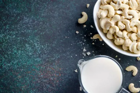 Cashewmilch selber machen ist einfach: Eine Schüssel voller Cashewkerne und ein Krug mit frischer Cashewmilch auf dunklem Untergrund.