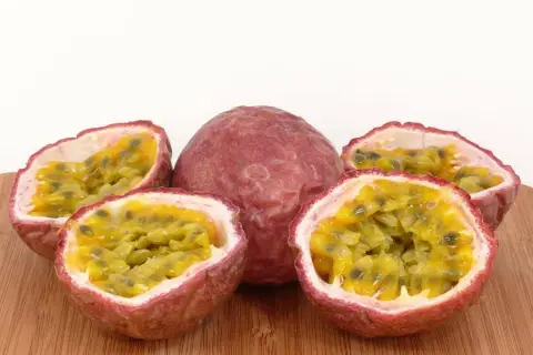 Ein ganzes und drei halbierte Passionsfrüchte liegen auf einem Holzbrett. Das Fruchtfleisch mit den Kernen lädt zum Passionsfrucht essen ein.