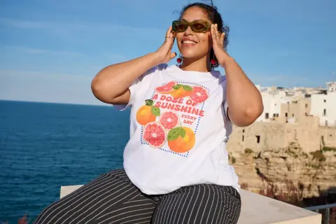 Frau mit Zitrusfrüchten-T-Shirt und gestreiften Hosen, perfekt für eine **capsule wardrobe sommer**.