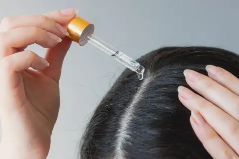 Eine Hand trägt mit einer Pipette ein Öl auf die Kopfhaut auf. Ein natürliches hausmittel gegen schuppen und juckende kopfhaut.
