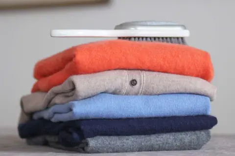Ein Stapel bunter Pullover, was ist Kaschmir? Weiche, luxuriöse Kleidung, die Pflege braucht. Ein Bürstchen liegt obenauf.