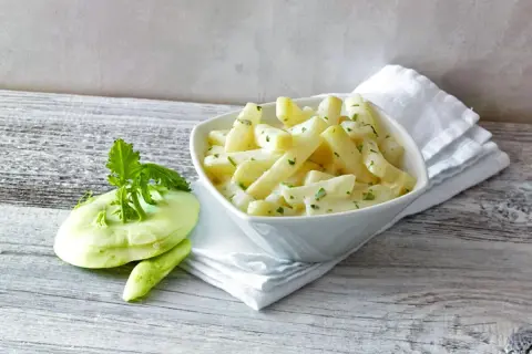 Schmackhafter Kohlrabi in cremiger Soße, daneben ein frischer Kohlrabi. Perfekt, wenn man wissen will, wie lange muss Kohlrabi kochen.