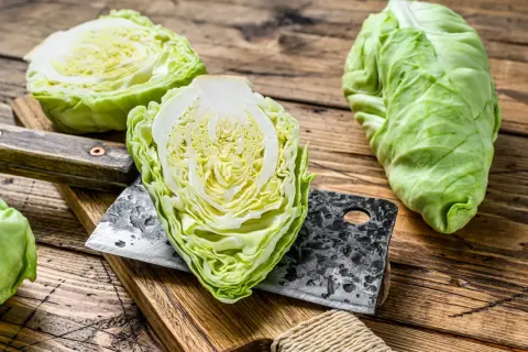 Frischer Spitzkohl, halbiert und auf einem Holzbrett mit einem Hackmesser. Perfekt, um Spitzkohl roh zu essen, als knackiger Salat.